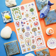 🍋🦞 Ciao to sunny days, seaside snacks, and a table full of color! This playful sheet is packed with lemons, tomatoes, seafood, spritzes, sardines, patterned tiles, and plenty of Mediterranean flair. Add in a few artsy portraits and bright floral details, and it’s basically a whole summer getaway squeezed onto one sticker sheet.

Top Coating: None
Adhesive Layer: PVC (plastic)
Backing Layer: Clear
6.69" x 3.54".
Weight - 0.03lbs
1 sheet included