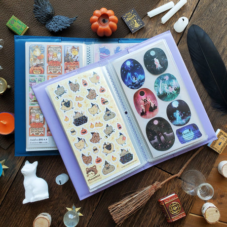 Time to add a little magic to your sticker stash! ✨ Our new Halloween duo has arrived — two perfectly spooky (and irresistibly cute) organizers ready to keep your collection spellbound all season long. Whether you're brewing up cozy crafts or flying into spooky season fun, these organizers will keep your collection safely tucked away in style! 💫

Each organizer features a vegan leather cover with a shimmering gold foil emblem and holds up to 48 sticker sheets across 24 pages.