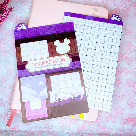 Sakuradragon - Sakura Street A6 Pencil Board

A napping Sakuradragon perched onto of a cozy little shop Sakura Street. It's almost as if she is sleeping on top of your notebook.

What is a pencil board?
Pencil boards are inserts for your notebook that sit under the page you are writing on. They prevent indents on the next page when you write and even prevent ink from bleeding through to the page beneath. But honestly, they can just be cute bookmarks.