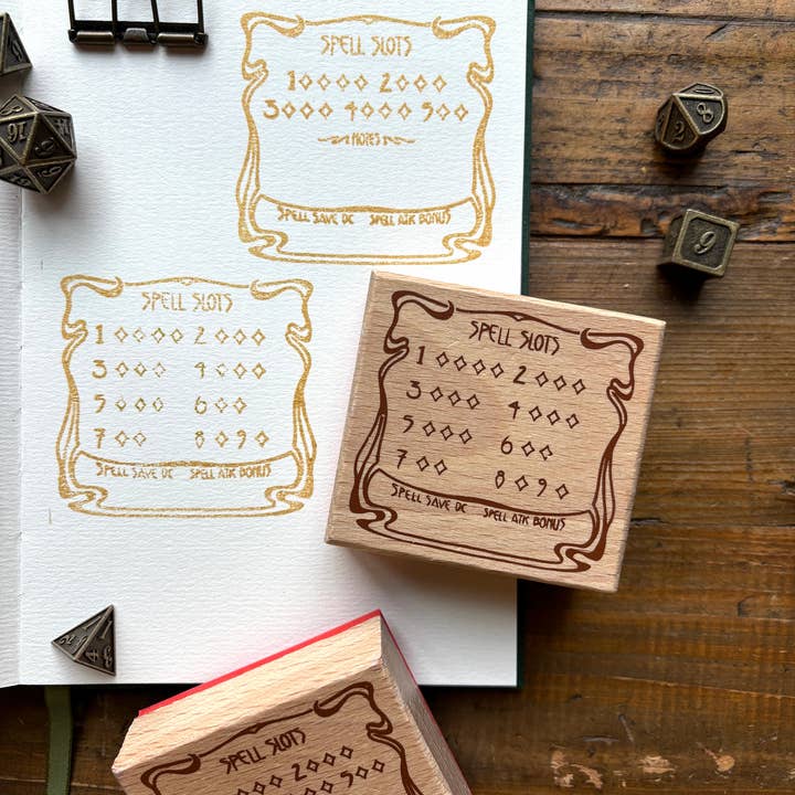 A collection of beech wood rubber stamps with gold detailing, used for tracking DnD spell slots, placed on a notebook and a red box.