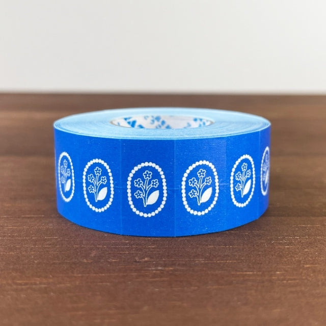 Stamp Marche Label Sticker Roll - Flower Brooch Blue Blue tape with white floral designs on a wooden surface