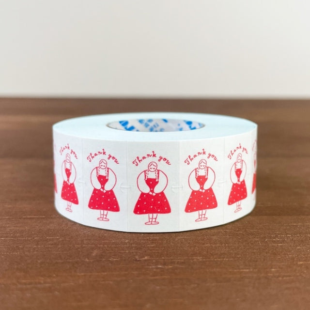 Roll of tape with red illustrations and 'Thank you' text on a wooden surface