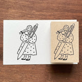 Stamp Marche Maru-Chan Uni-ball Wooden Stamp Rubber stamp with a design of two figures holding a large pen on a wooden surface.