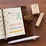 Stamp Marche Maru-Chan Uni-ball Wooden Stamp Notebook with stationery items including a pen and rubber stamps on a wooden surface