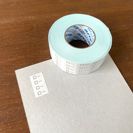 Stamp Marche Planner Label Sticker Roll - Checkbox Roll of checkered tape with a sample label on a wooden surface