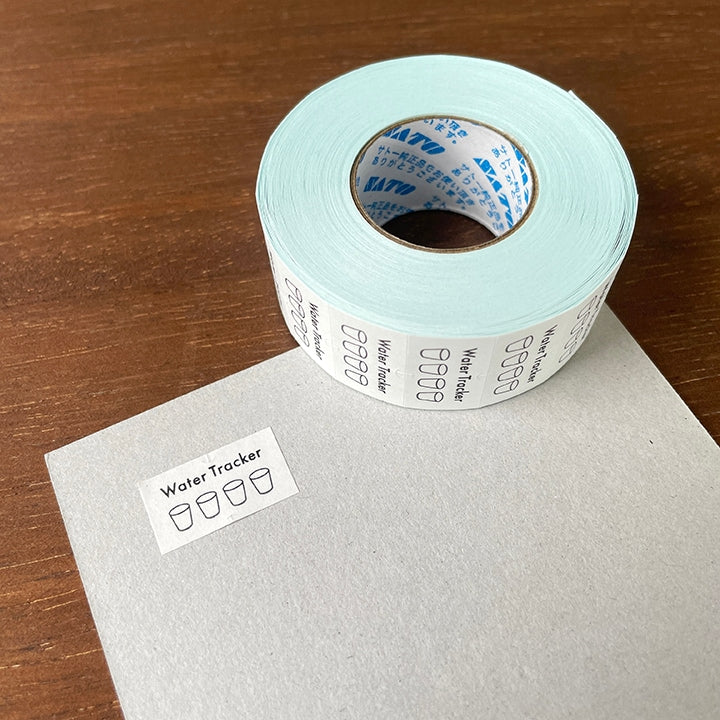 Stamp Marche Planner Label Sticker Roll - Water Tracker Roll of water tracker labels on a wooden surface
