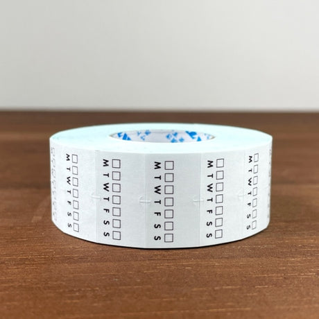 Stamp Marche Planner Label Sticker Roll - Weekly Habit Tracker Roll of tape with calendar markings on a wooden surface