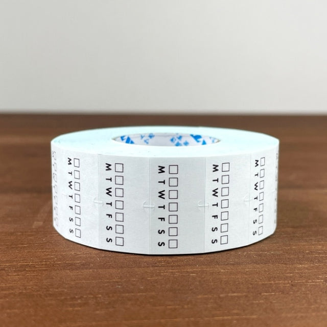 Stamp Marche Planner Label Sticker Roll - Weekly Habit Tracker Roll of tape with calendar markings on a wooden surface