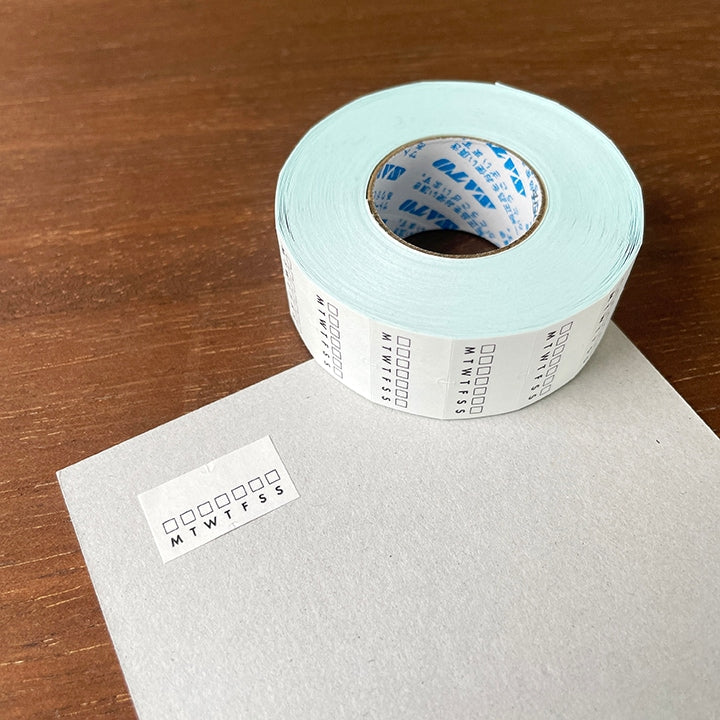 Stamp Marche Planner Label Sticker Roll - Weekly Habit Tracker Roll of pre-printed labels on a wooden surface