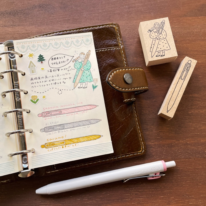 Notebook with stationery items including a pen and rubber stamps on a wooden surface Stamp Marche Uni-ball One Wooden Stamp