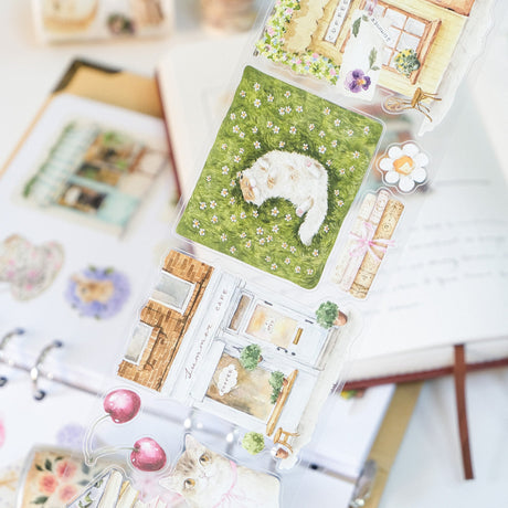 Step into a world where nature and comfort collide. Our Summer Café Wide Tape transforms your stationery into a bustling garden bistro, teeming with life, blooming flowers, and the true owners of the cafe: the cats.

This whimsical design weaves together the architecture of charming coffee shops with the wild beauty of summer florals. Nestled among the potted plants and open doors, you’ll find hand-painted cats exploring, sleeping, and playing.&nbsp;

