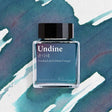 A cold teal greenish blue reminiscent of deep sleep is veiled with muted violet that softly blooms across the surface, capturing the love first encountered by Undine, a being once born of water, and the quiet tragedy that followed in its wake.