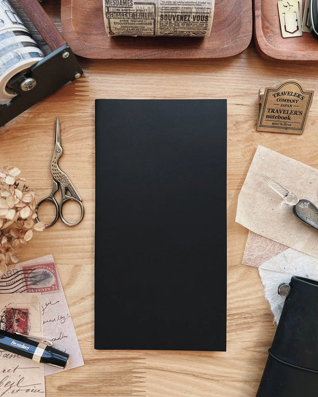Black notebook on a wooden surface with stationery items