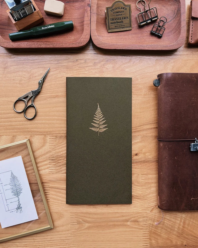 Green notebook with a leaf design on a wooden surface with stationery items.