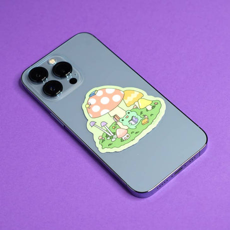 Pegatina de rana leyendo entre hongos